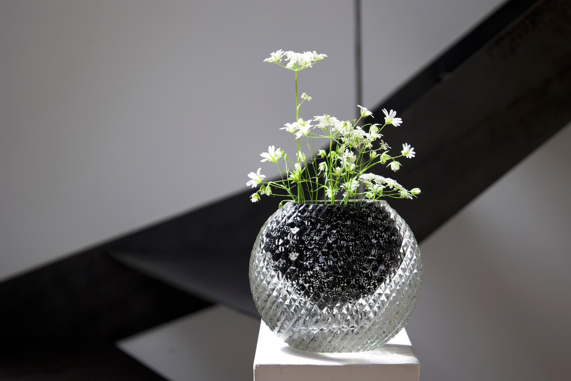 A cut-glass vase holding delicate white wildflowers, displayed on a white pedestal.