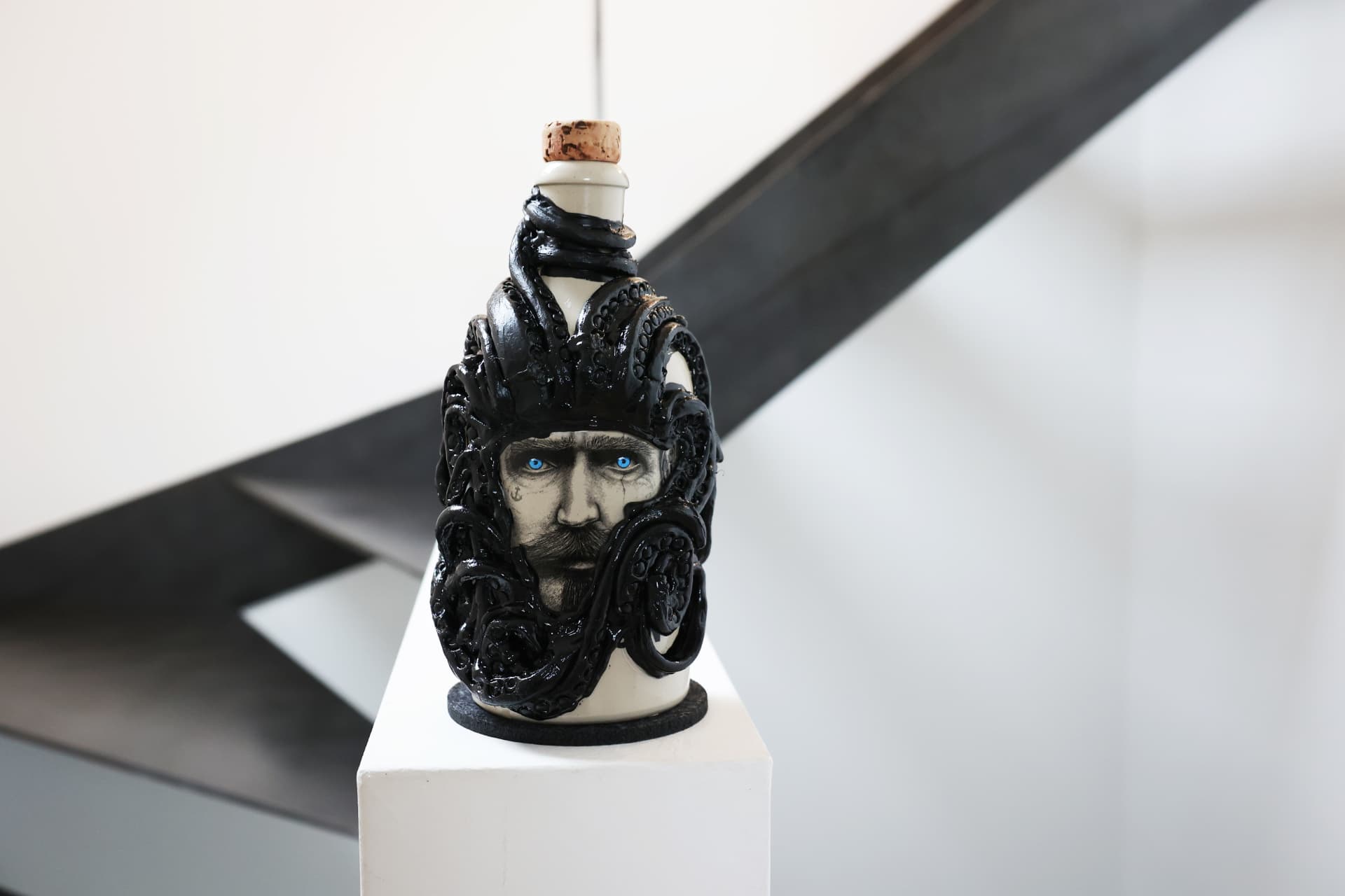 A Kraken rum bottle sculpture with sculpted black tentacles wrapped around the vessel, displayed on a white pedestal.