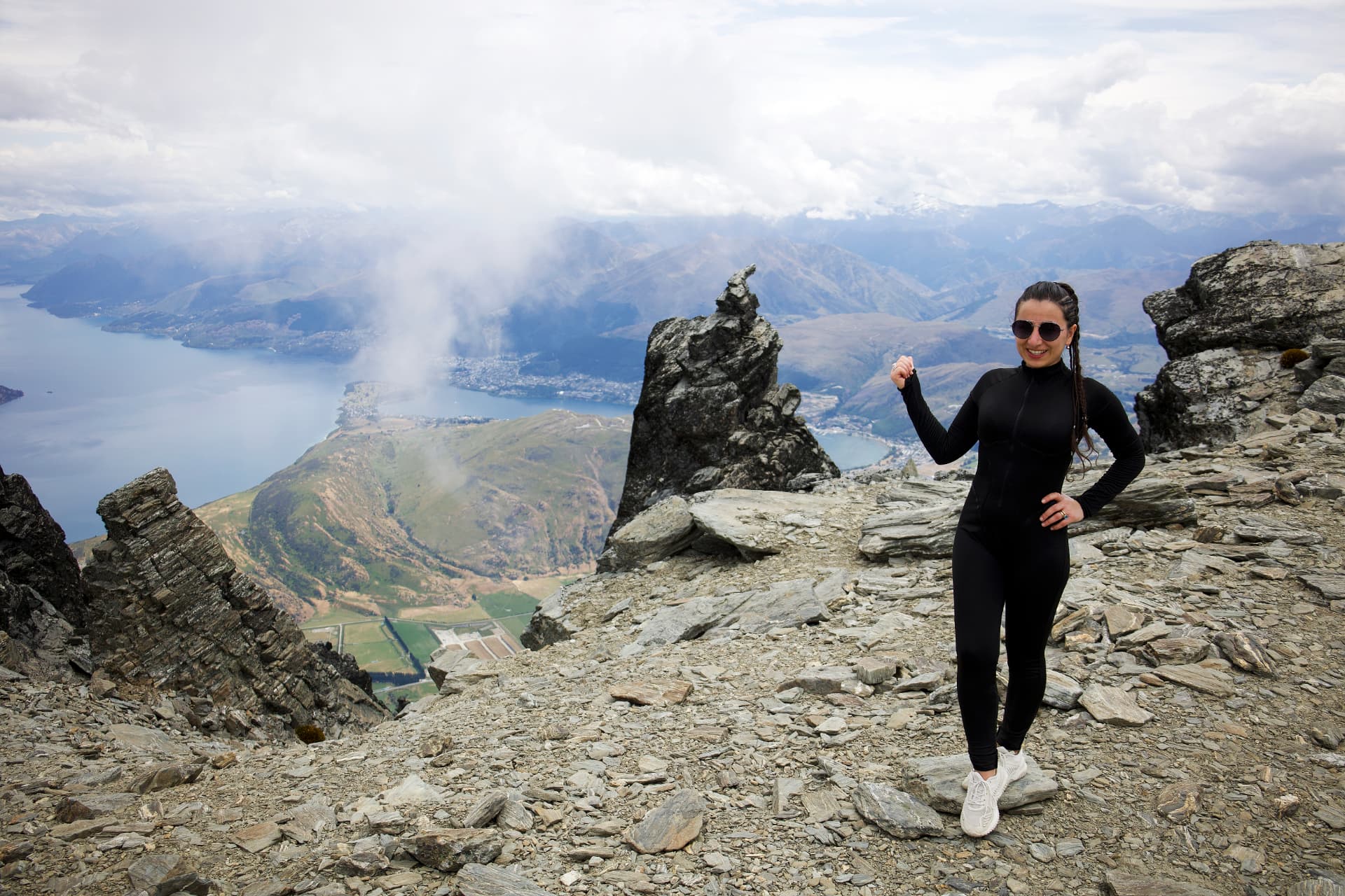 Ashkhen Zakharyan standing on a rocky mountain summit with a lake and valleys in the background