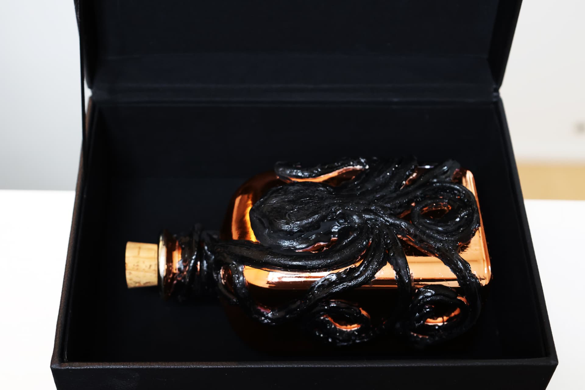 A copper-colored Kraken rum bottle sculpted with dark tentacles, lying inside an open black luxury box.