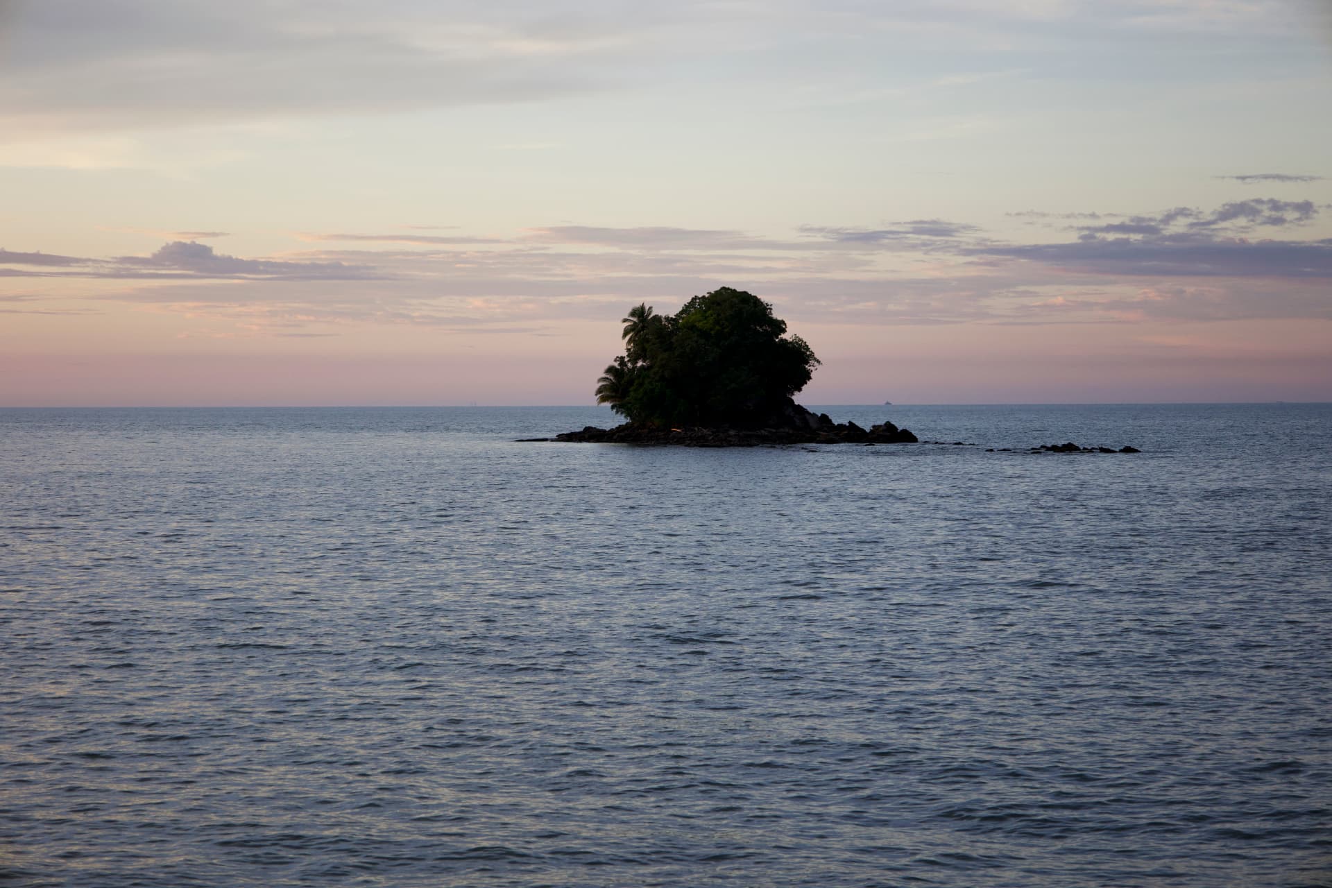 A small tree-covered island at sunset in calm waters off Kampong Jerudong, Brunei