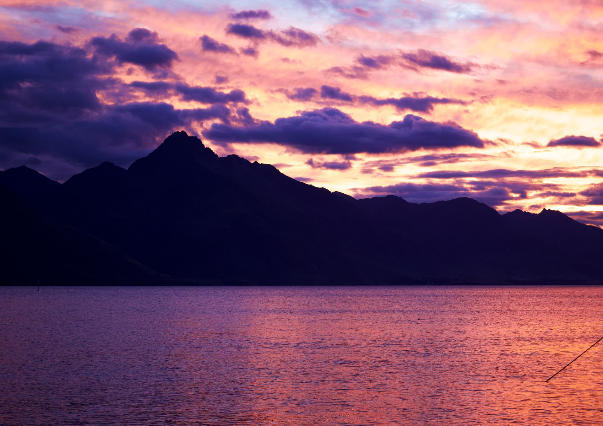 A purple and orange sunset over Lake Wakatipu with mountain silhouettes, Queenstown, New Zealand