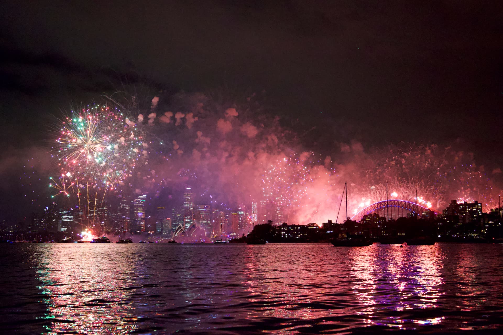 Colourful New Year fireworks over Sydney Harbour with the Opera House, Harbour Bridge and city skyline reflected on the water