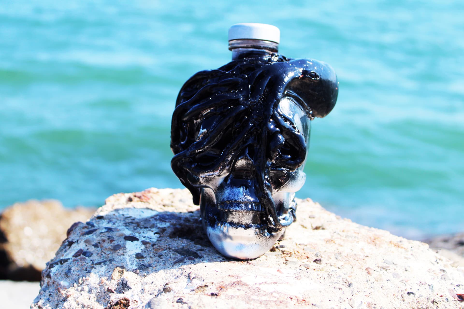 A black Kraken rum bottle sculpted with sprawling tentacles, perched on a seaside rock against bright blue water.