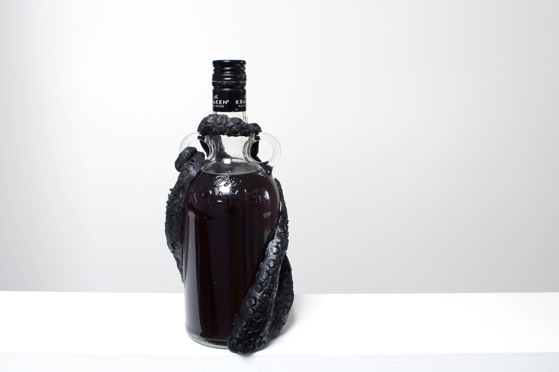 A black Kraken rum bottle with sculpted dark tentacles coiled around its neck and body, standing against a plain white background.